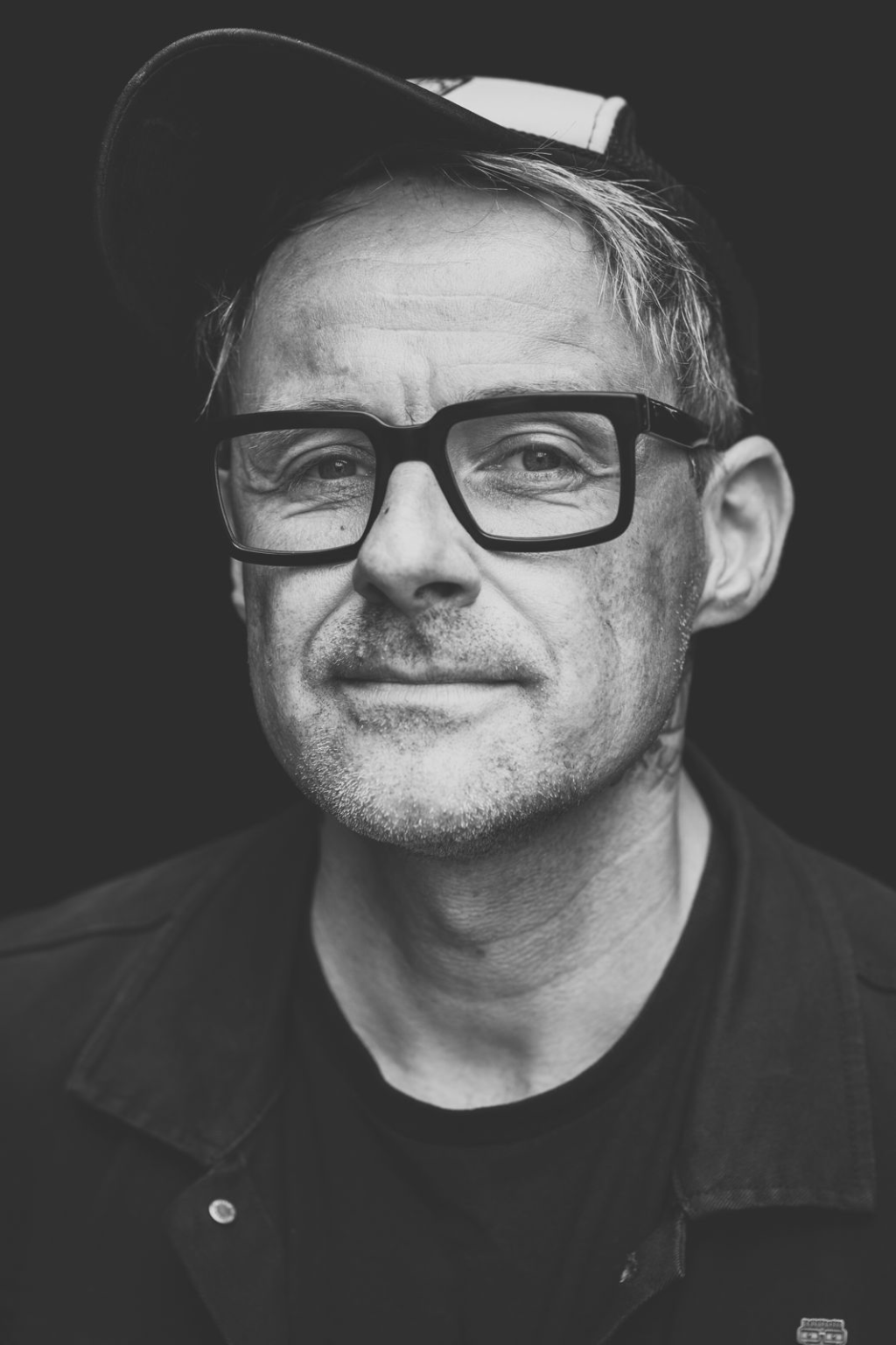 Foto von Ingo Donot mit Basecap und dickrandiger Brille, neutraler Blick, Schwarzweiß-Porträt